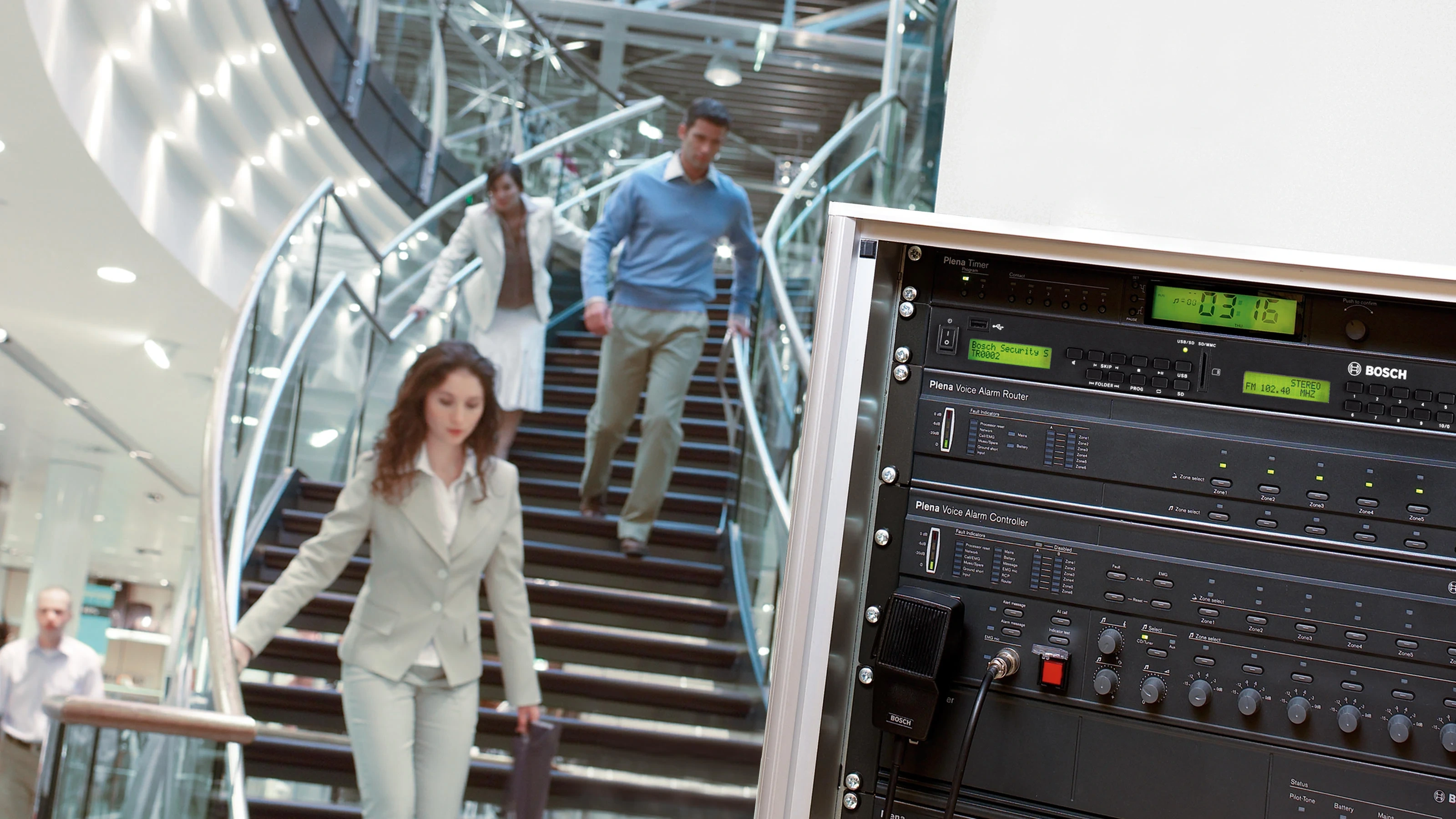 Bosch PLENA voice alarm rack in a building lobby with people on a staircase